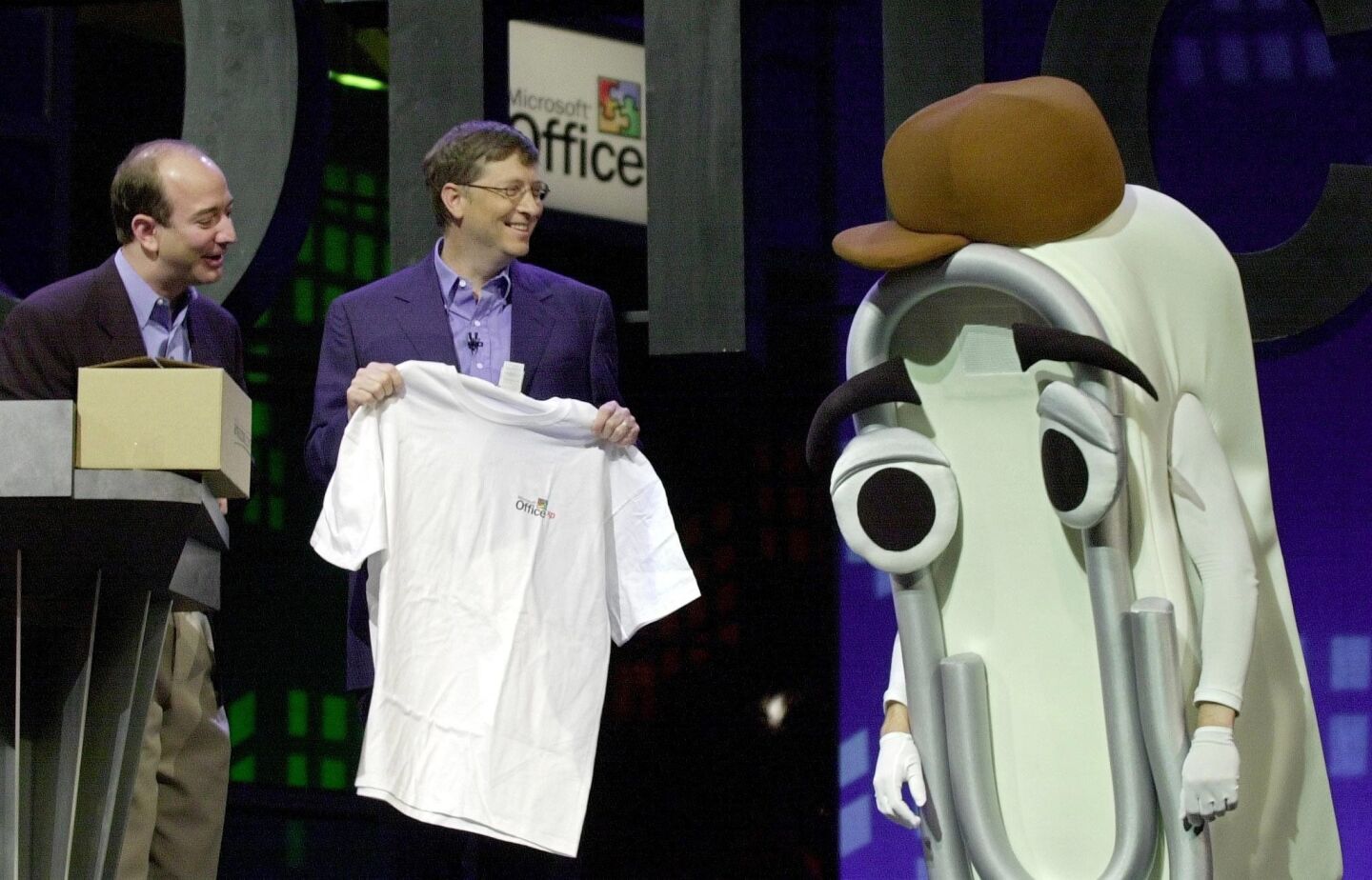Microsoft CEO Bill Gates presents a T-shirt as a retirement gift to "Clippy," a person dressed as the Microsoft Office Assistant, as Amazon.com CEO Jeff Bezos looks on at the Office XP launch, May 31, 2001, in New York.