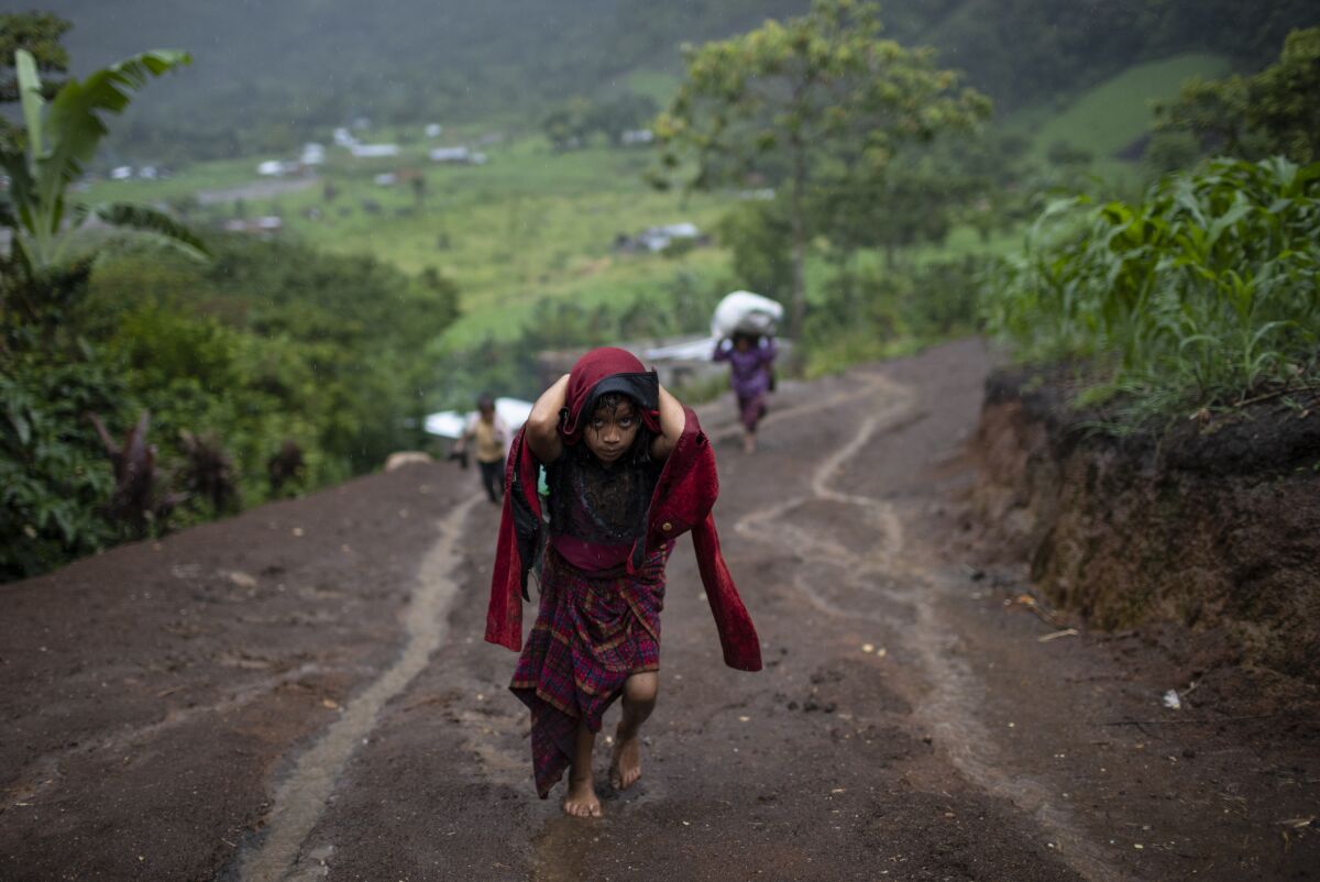 After a heavy rain, a girl hauls wood for cooking, in the makeshift settlement Nuevo Queja, Guatemala, Monday, July 5, 2021. The survivors of a mudslide triggered by Hurricane Eta, burying their Guatemalan town Queja in November 2020, were left destitute and displaced in the desperately shabby settlement. (AP Photo/Rodrigo Abd)