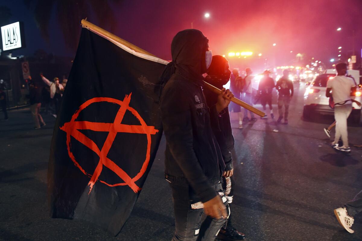 A man carries a flag depicting the anarchist symbol during a public disturbance Saturday on Melrose Avenue in Los Angeles.