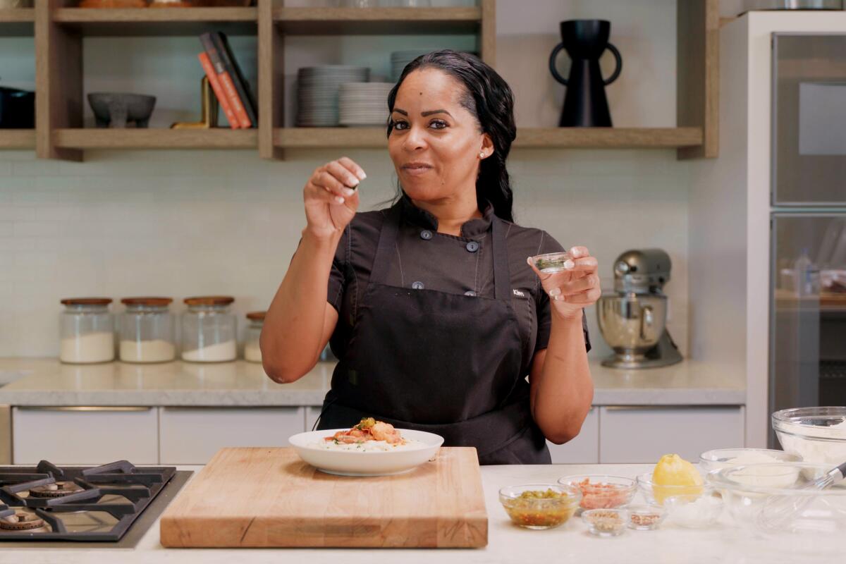 A woman in a kitchen seasoning a plate of shrimp and grits.