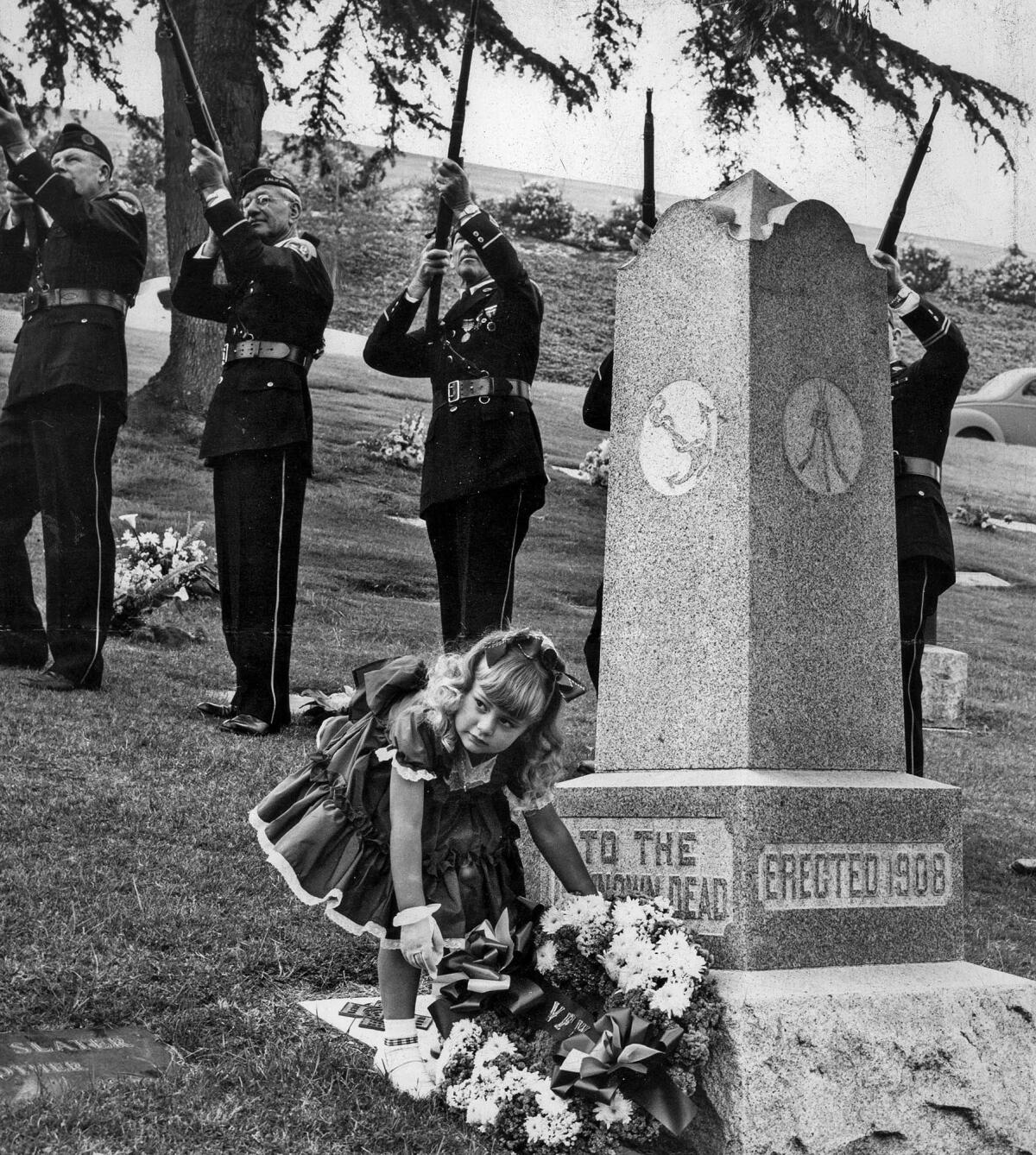 May 30, 1954: Kristy Kyte, 3, places a wreath on a monument to the unknown dead at Rose Hills Memorial Park while members of Legion Post 51 prepare to fire.