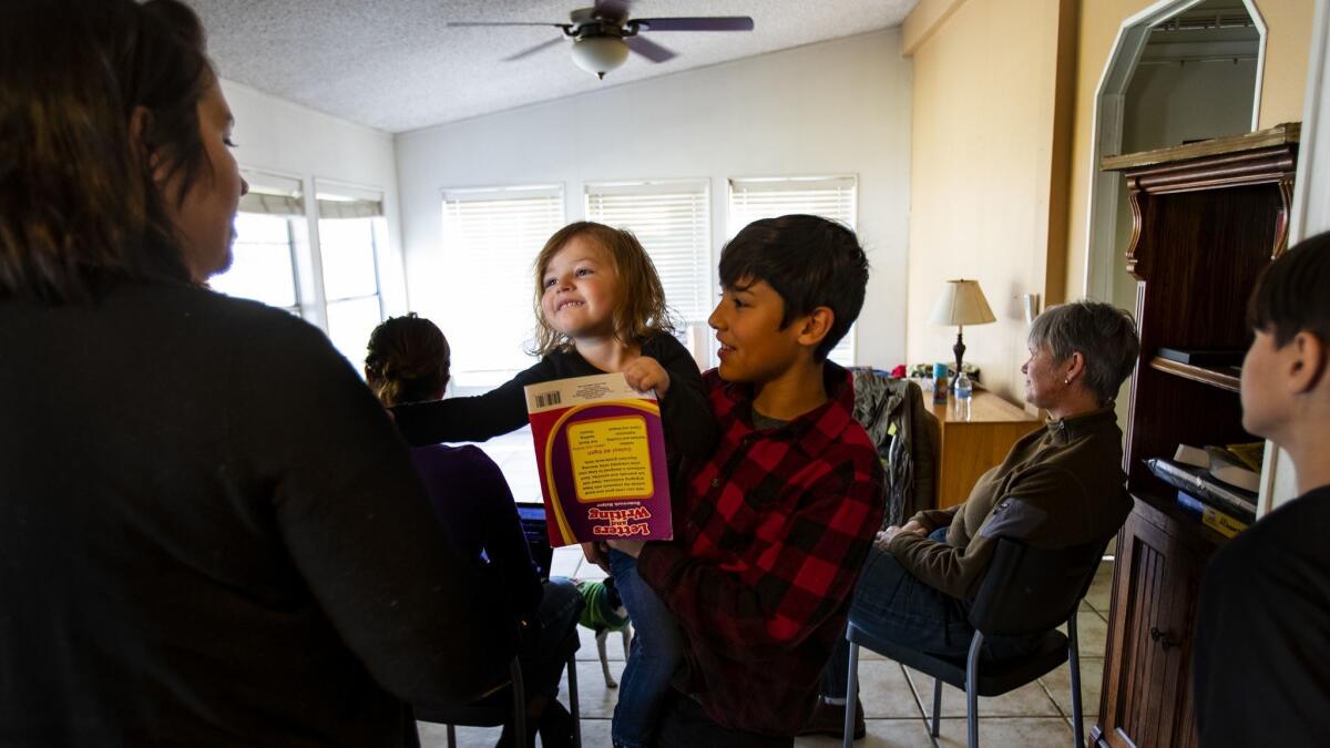 Camp fire evacuee Gage Smith hands his sister Willow Wood to his mother, Desiree Kilpatrick, left, inside the home of Gina Muse, who took them in when they had nowhere to go.