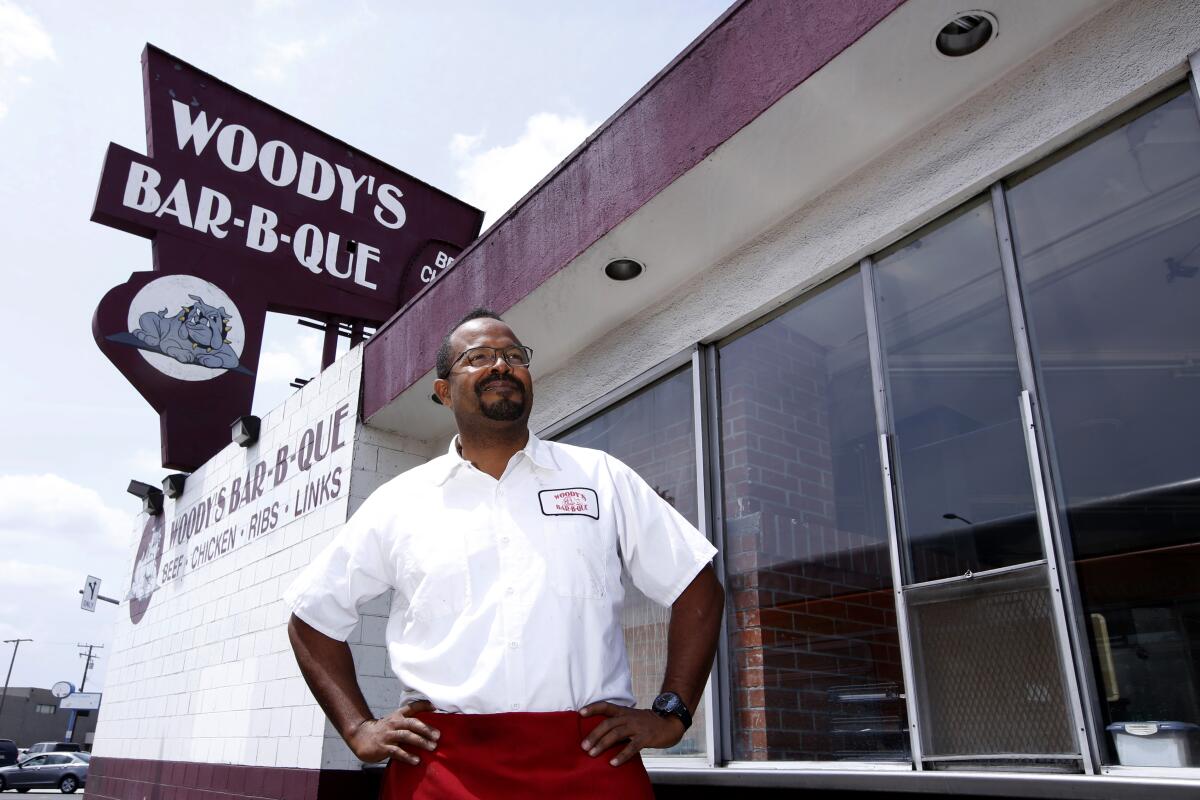 A man stands outside a building under the sign Woody's Bar-B-Que