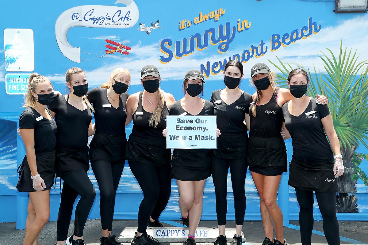 Cappy's Cafe waitresses wear plastic gloves and face masks and hold a sign provided by the Newport Beach Chamber of Commerce.