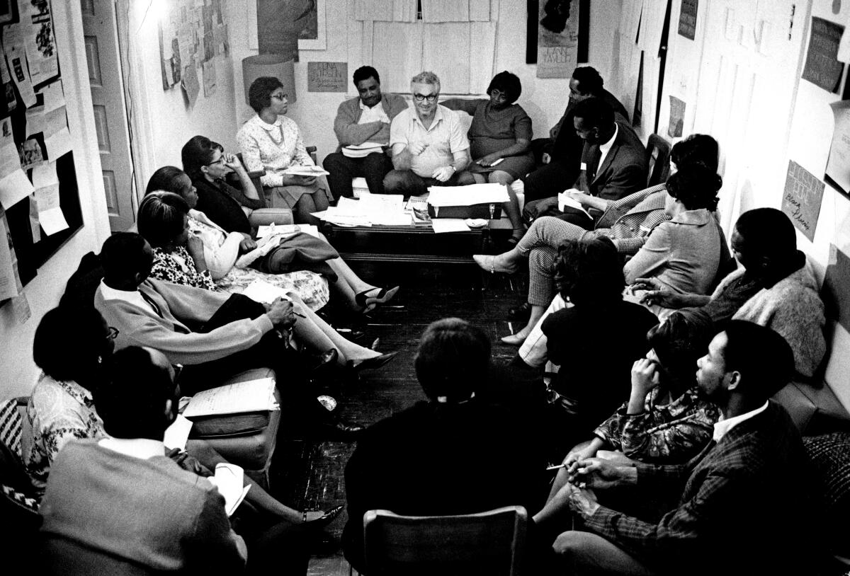 A black and white photo of a group of men and women sitting in a circle