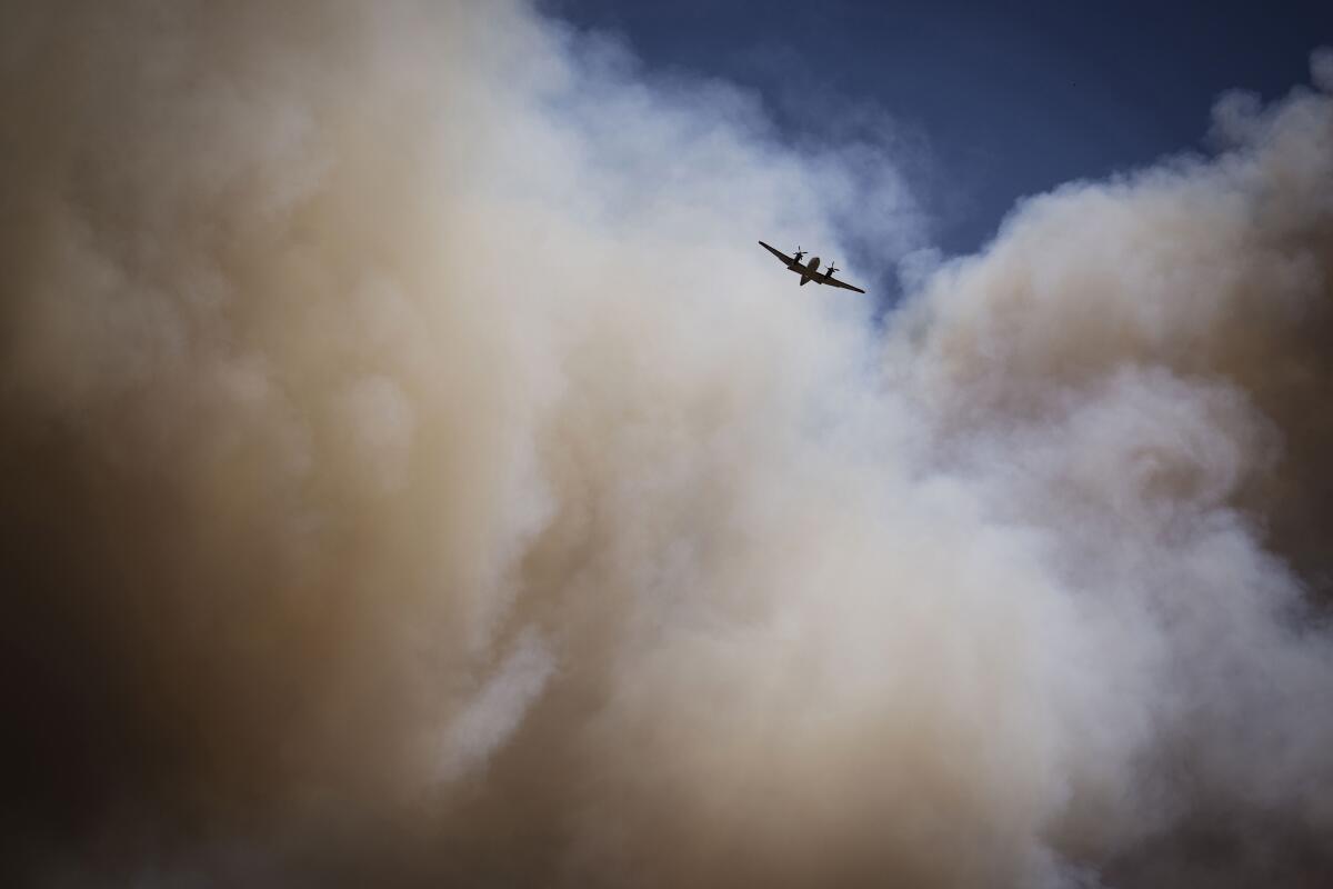 An air tanker soars through a large plume of smoke 