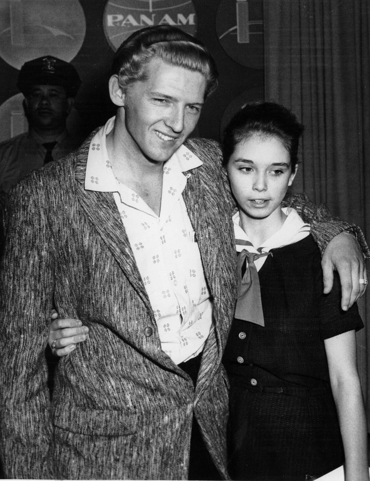 A black-and-white photo of a man with his arm around the shoulder of a teenage girl.