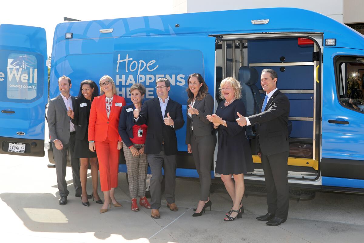 Elected officials stand in front of a Be Well OC mobile vehicle at Huntington Beach Civic Center Plaza.