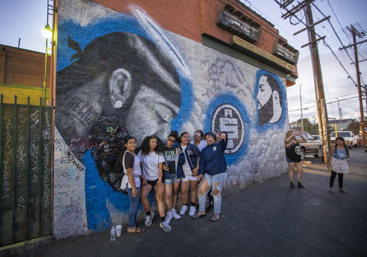Tourists pose in front of a mural of slain rap star Nipsey Hussle.