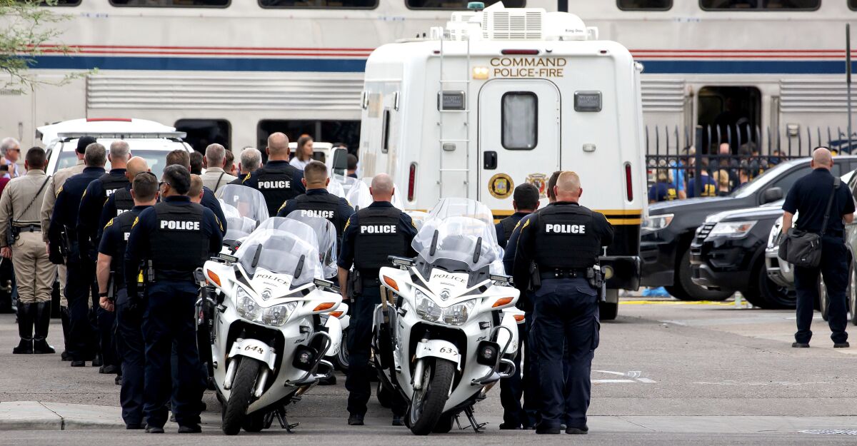 Tucson Police officers and other law enforcement officers stand at attention as the body of a Drug Enforcement Administration special agent is removed from an Amtrak train and loaded into a van from the Pima County Medical Examiner following a shooting Monday, Oct. 4, 2021, in Tucson, Ariz. (Rebecca Sasnett/Arizona Daily Star via AP)