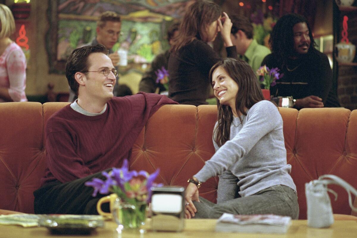 Matthew Perry as Chandler Bing sits next to Courteney Cox as Monica Geller on Central Perk's iconic orange couch