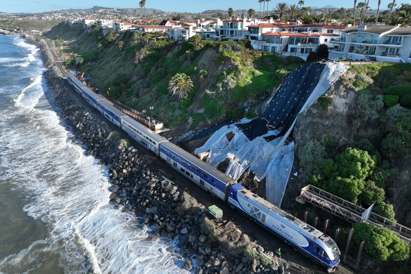 San Clemente, CA - March 08: An aerial view of Amtrak Pacific Surfliner resuming service while passing through the repaired tracks and barrier wall construction at Mariposa Point in San Clemente Friday, March 8, 2024. Rail service is on a limited basis. The reopening of the line this week marked the first time in more than a month that passengers have been able to hop aboard Amtrak's Pacific Surfliner and ride through the coastal swath between Orange County and San Diego. Construction continues on the barrier wall, which will be 10 to 15 feet high and 192 feet long. A series of powerful winter storms saturated the hillside adjacent to the tracks, causing it to slide and crumble, and forcing officials to halt train service for weeks. (Allen J. Schaben / Los Angeles Times)