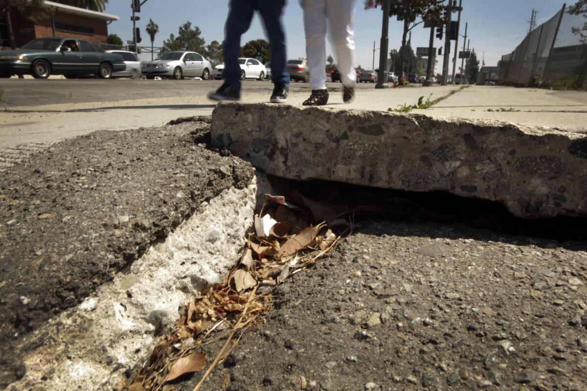 Two people navigate a buckled sidewalk along Vermont Avenue at the 101 Freeway.