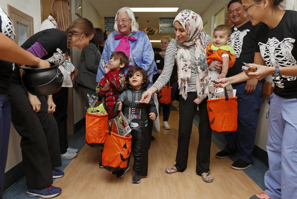 Nouraldeen Kaskas, 4, center, wearing a Darth Vader costume, his brother Mohammad, 6, dressed as Iron Man, and their mother, Rawan, right, receive Halloween treats from doctors and staff members in the pediatric ward of Fountain Valley Regional Hospital & Medical Center on Thursday during a daytime trick-or-treat parade.