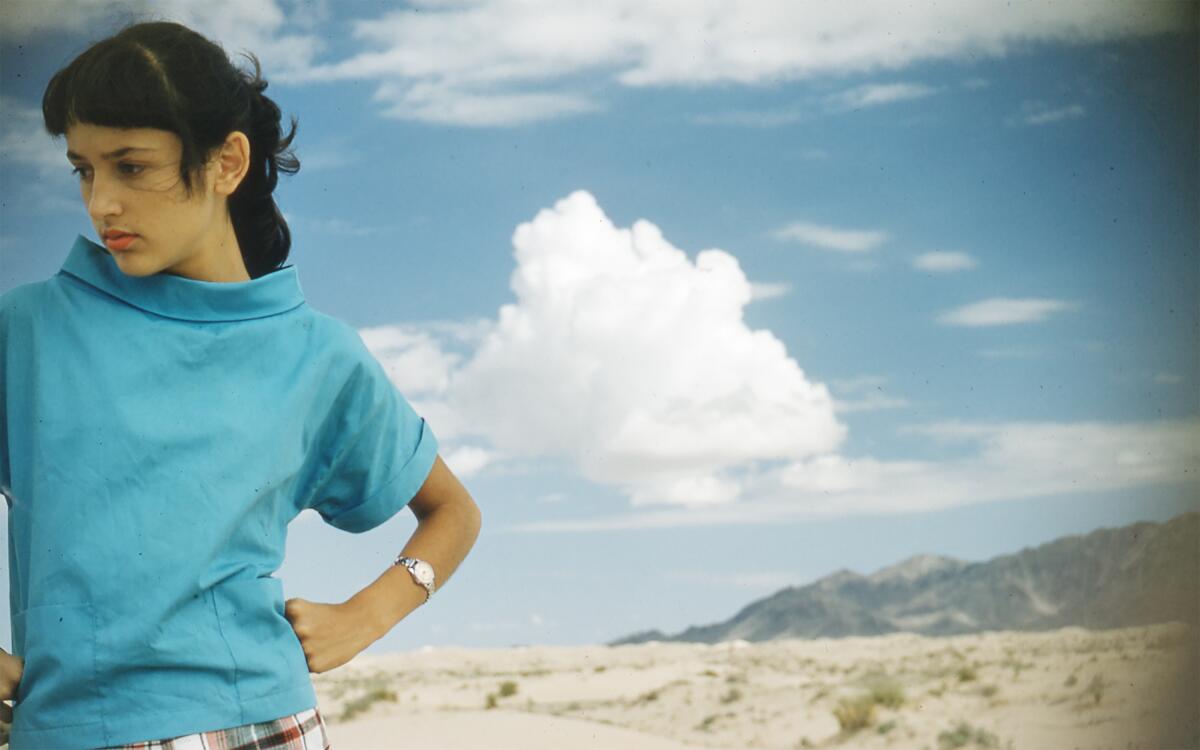 A woman in a blue shirt with blue sky and clouds behind her