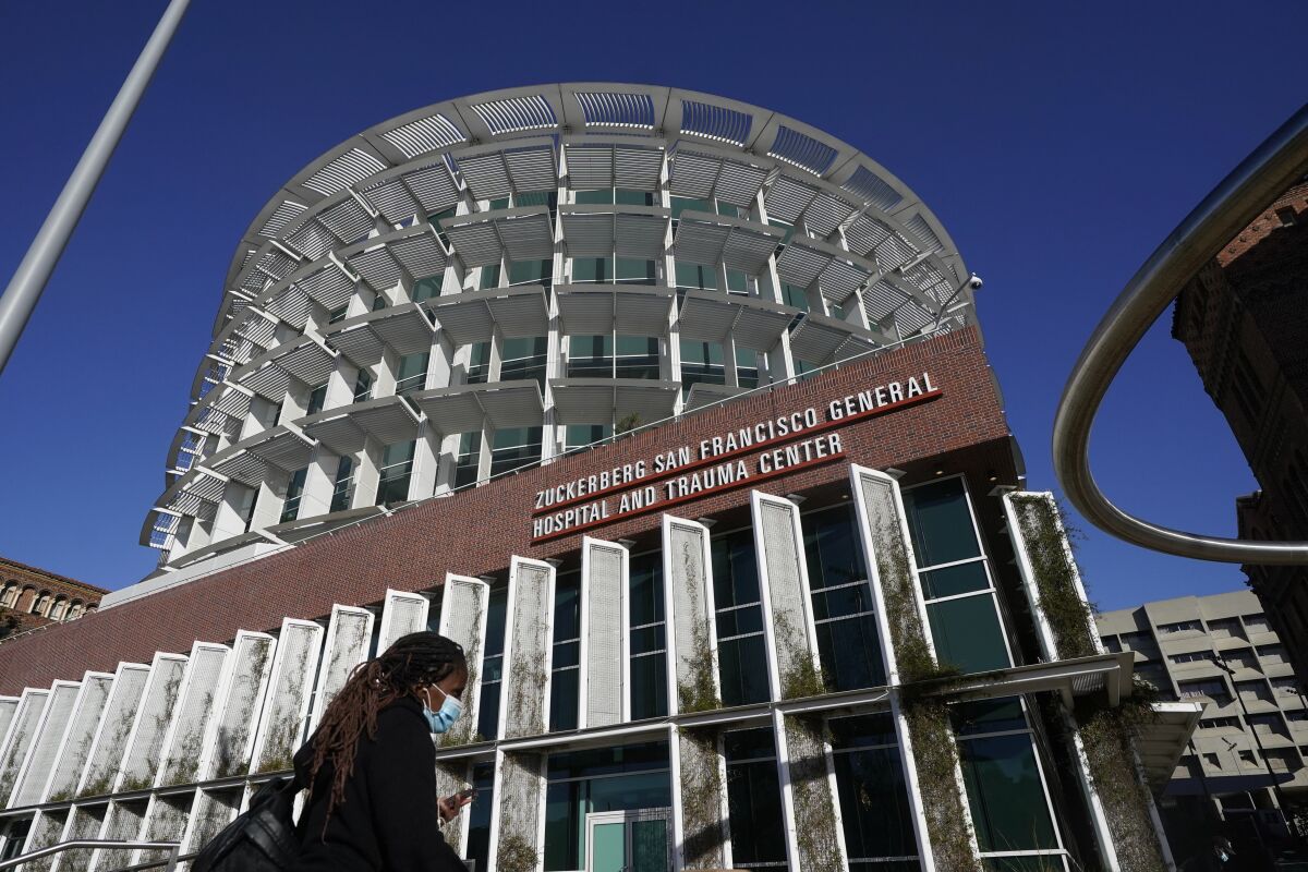 A woman wearing a mask walks under a sign for Zuckerberg San Francisco General Hospital and Trauma Center in San Francisco.