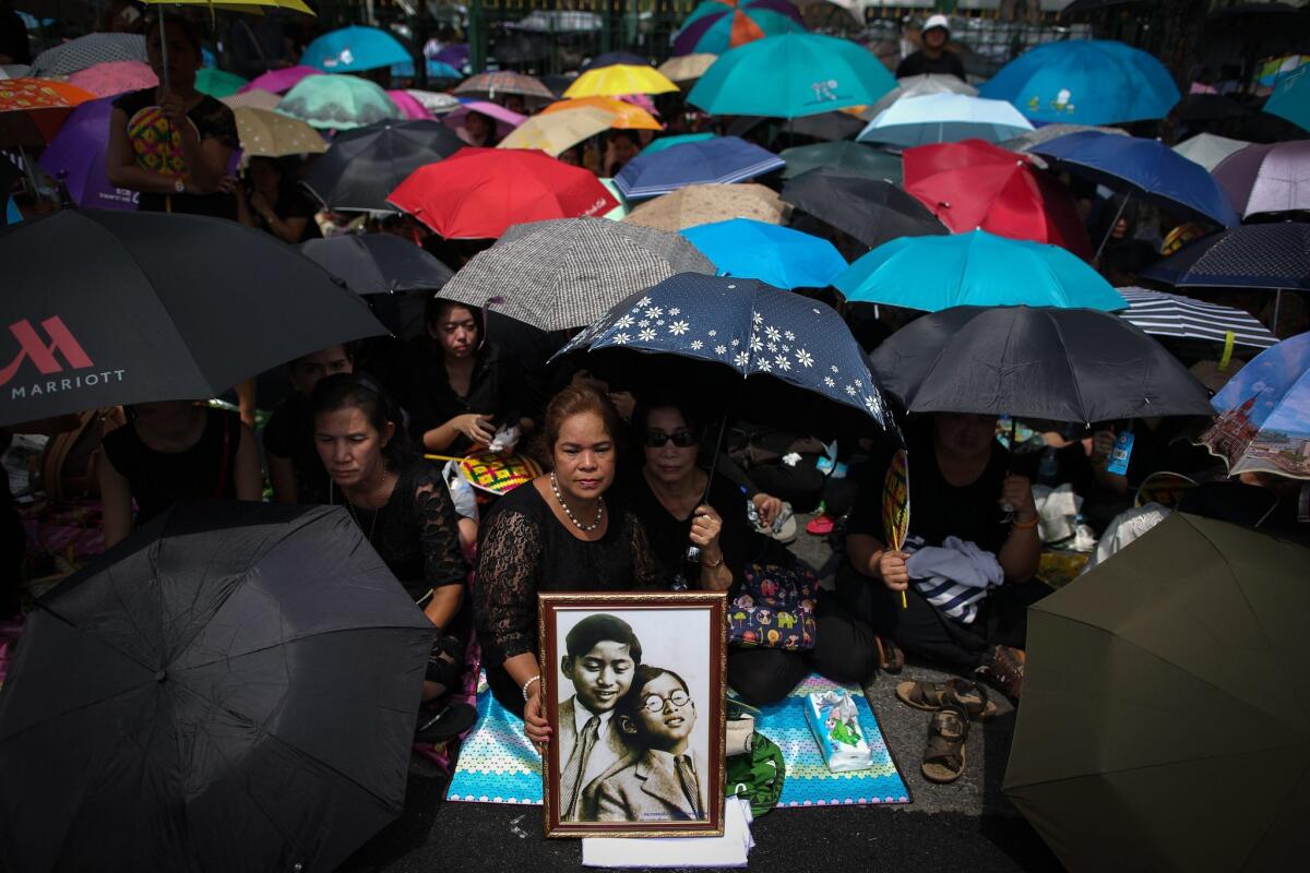 Thai mourners, holding a picture of their late King Bhumibol Adulyadej and his brother King Ananda Mahidol, wait for the procession carrying Adulyadej's body from Siriraj Hospital to the Grand Palace in Bangkok, Thailand, on Oct. 14, 2016.