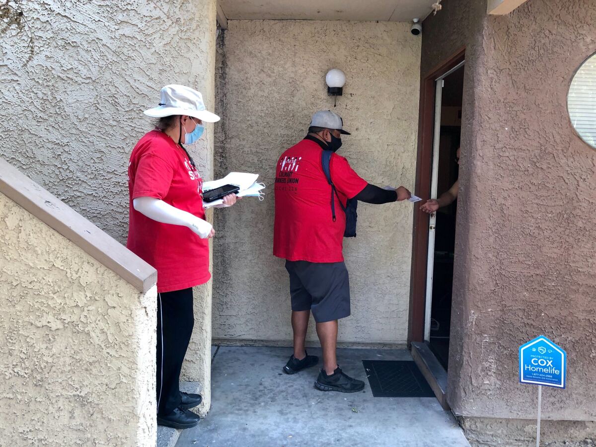 Two people in red shirts hand a pamphlet to a voter through their door