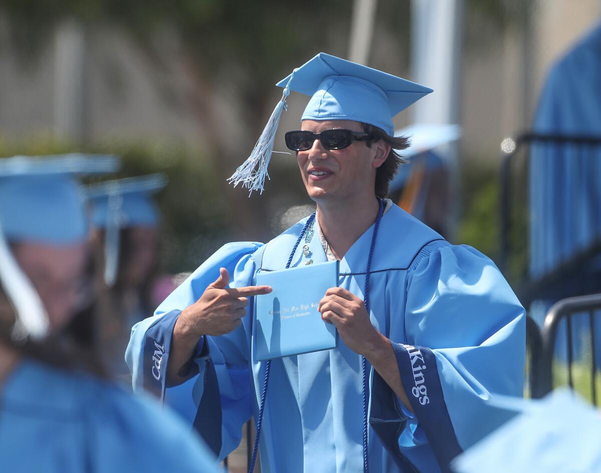 A new graduate points to his diploma as he walks down a ramp.