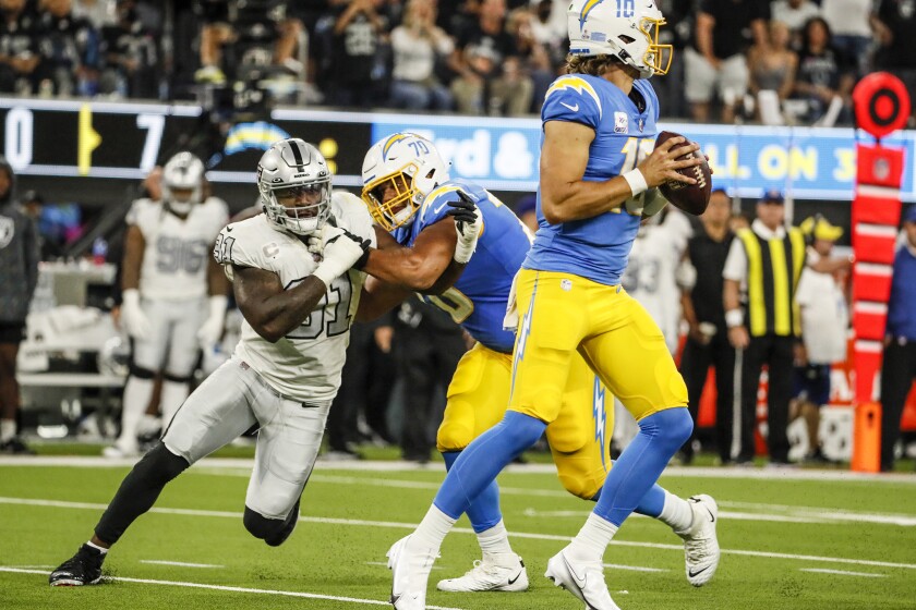 Chargers offensive tackle Rashawn Slater (70) fends off Raiders' Yannick Ngakoue (91) as Justin Herbert drops back to pass.