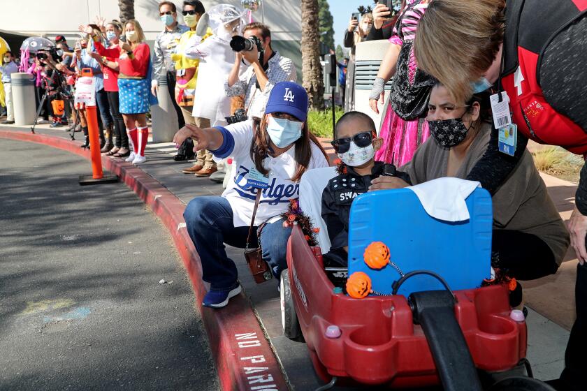 Alexander Vera, 3, sits in a wagon as he looks on with his mother Mayra Guadarrama, right, and Dr. Teresa Owens-Lim, left, director of Maternal Child Health Services, during the 14th annual Pediatric trick-or-treat parade at Fountain Valley Regional Hospital and Medical Center on Friday.
