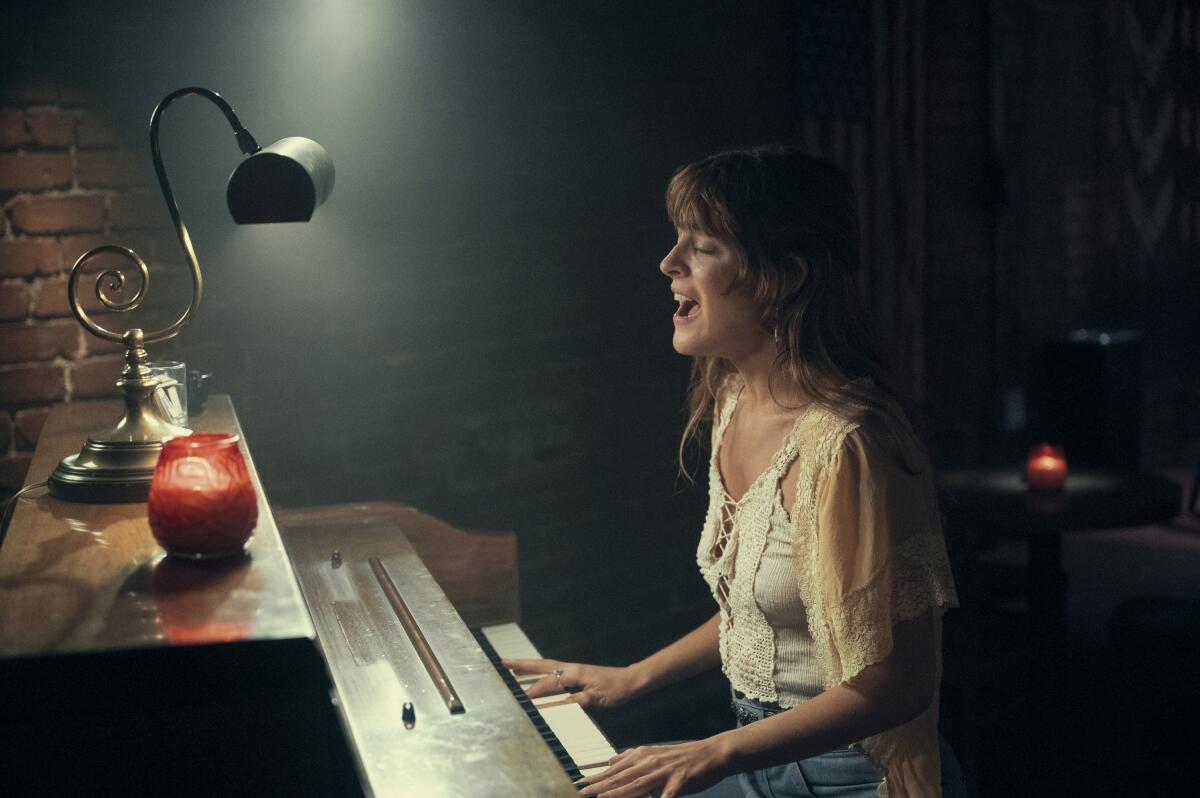 A woman sings at a piano in a dark bar.