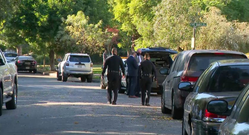 Two police officers walk outside near a row of parked cars.