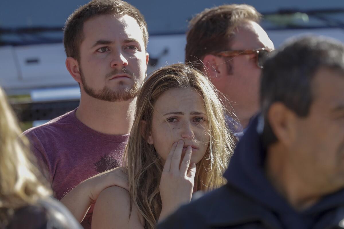 Harrison King, 24, and Alexis Tait, 23, stand on the roadside as a hearse carrying the body of Ventura County sheriff's Sgt. Ron Helus leaves in a procession. King and Tait escaped the shooting at Borderline, but one of their friends was killed.