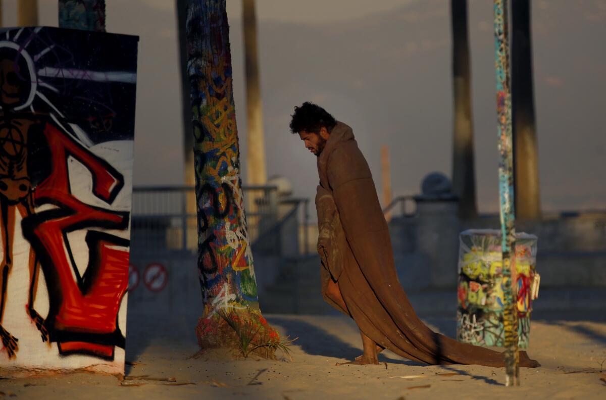 A homeless man walks around Venice Beach at dawn.