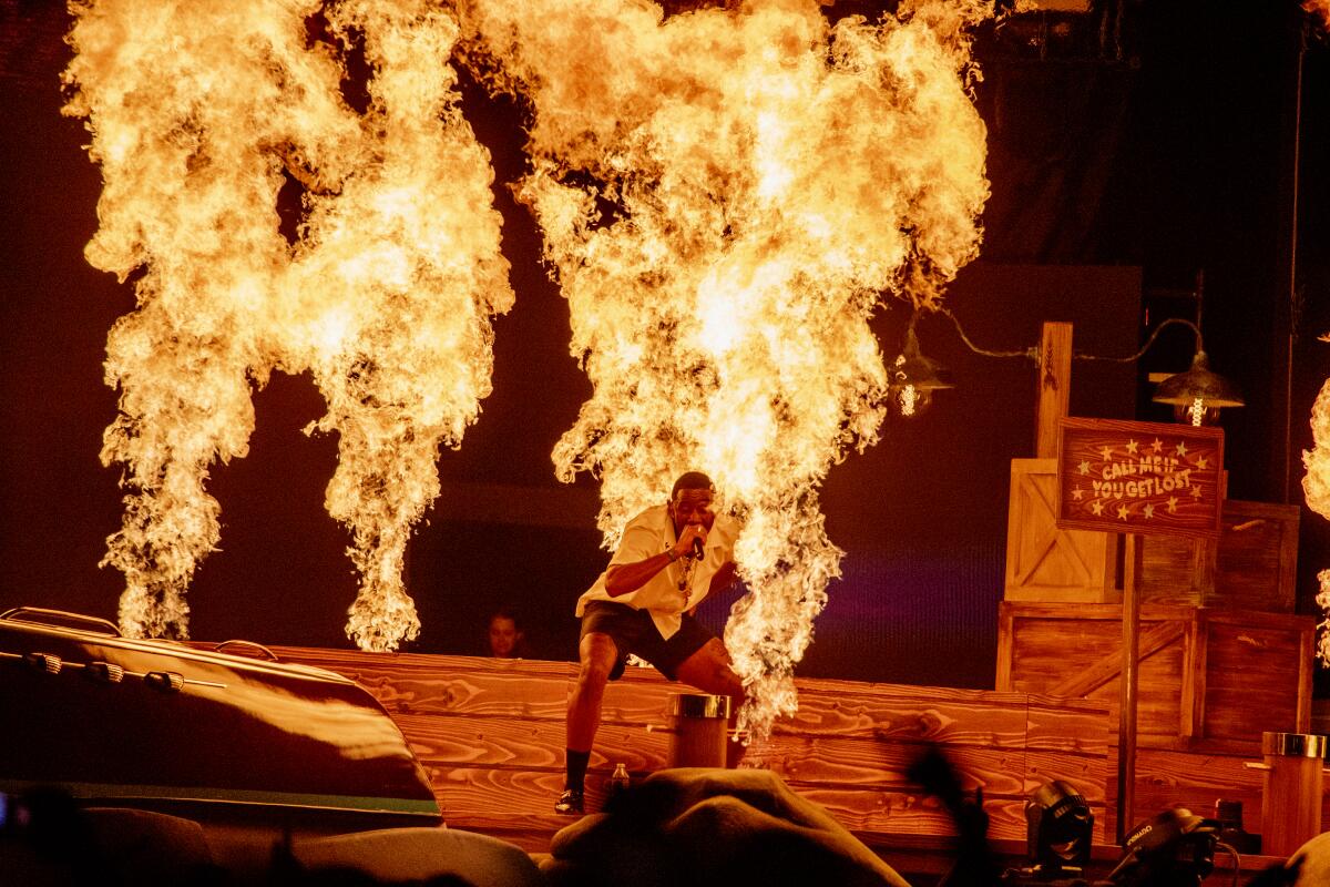 A rap artist performs onstage in front of flames shooting up from the stage