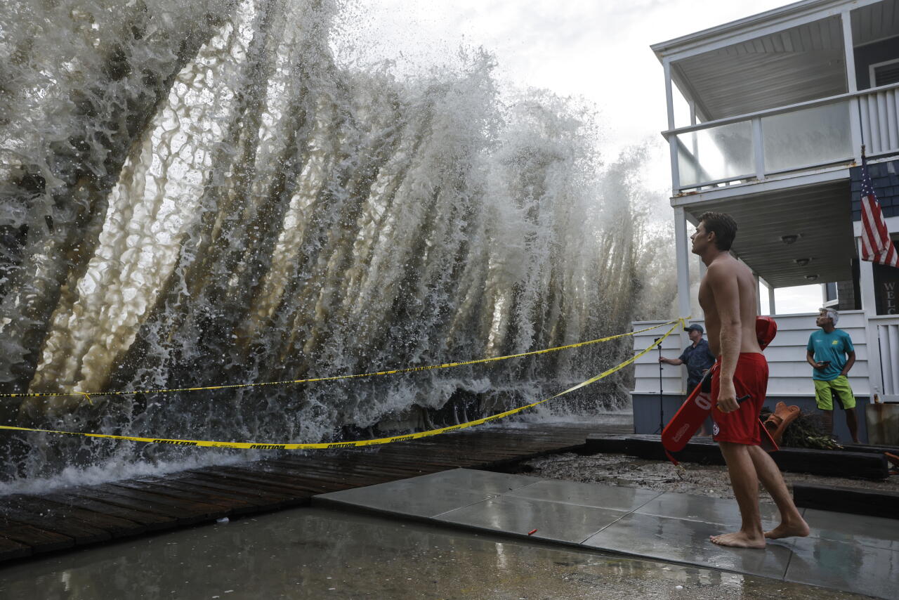 A lifeguard keeps watch along a closed boardwalk as a Pacific Ocean wave crashes over a seawall protecting homes