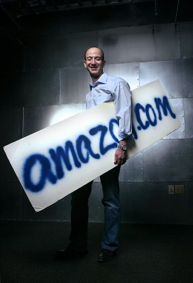 Jeff Bezos, founder, CEO and chairman of Amazon.com, holds the company's first sign, quickly spray-painted prior to an interview with a Japanese television station in 1995, at Amazon's Seattle headquarters.