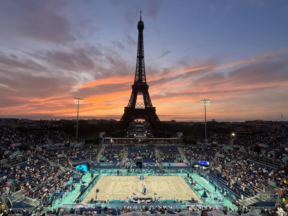 Spectators photograph a colorful sunset at Eiffel Tower Stadium prior to a beach volleyball match.