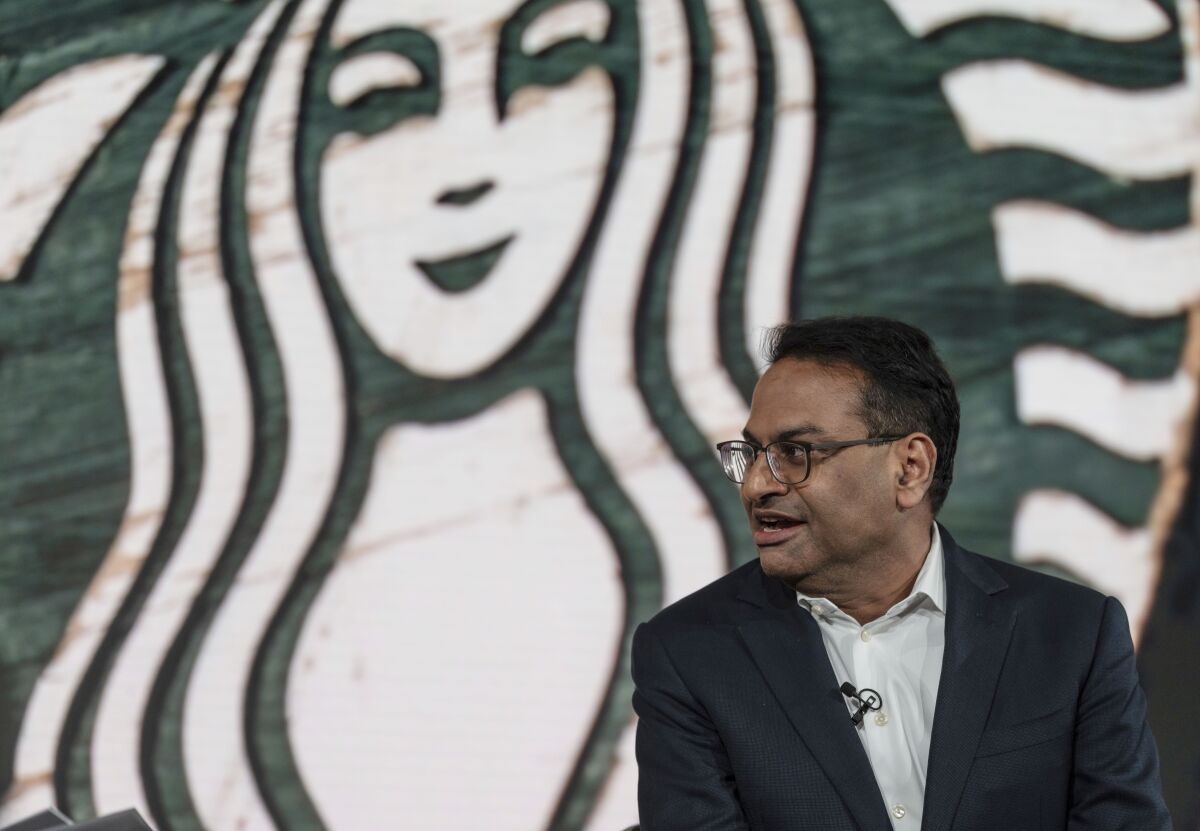 A man speaks in front of the Starbucks logo.