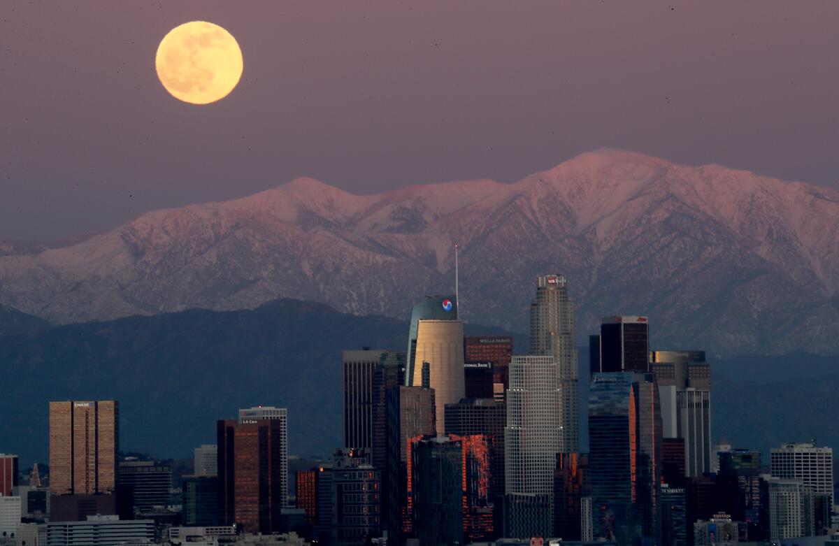 A full moon rises Tuesday, Dec. 29 over the snow-capped San Gabriel Mountains and the skyline of downtown Los Angeles.