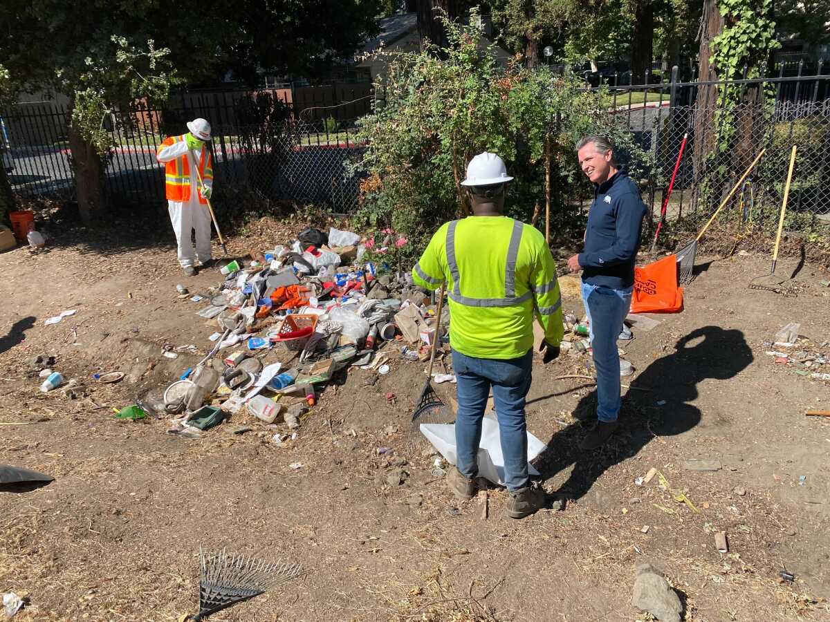 Gov. Gavin Newsom and two workers around a pile of stuff.