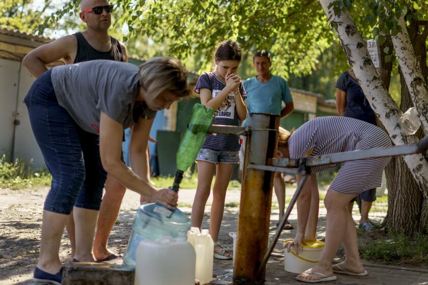 Residents gather to pump water from a well outside an apartment complex in Sloviansk, Donetsk region, eastern Ukraine, Saturday, Aug. 6, 2022. Fighting between Ukrainian and Russian forces near the key city has damaged vital infrastructure that has cut residents off from gas and water for months. The water continues to flow for now, but fears grow that, come winter, the city only seven miles (12 kilometers) from Russian-occupied territory could face a humanitarian crisis once the pipes begin to freeze over. (AP Photo/David Goldman)