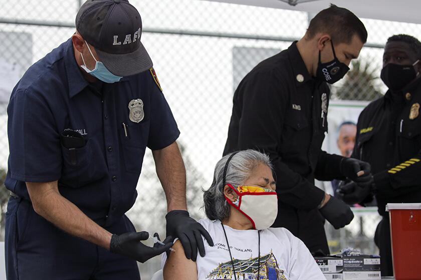 Firefighter Anthony MacDougall administers a COVID-19 vaccine to Carmen Limeta at a mobile vaccination site in L.A.