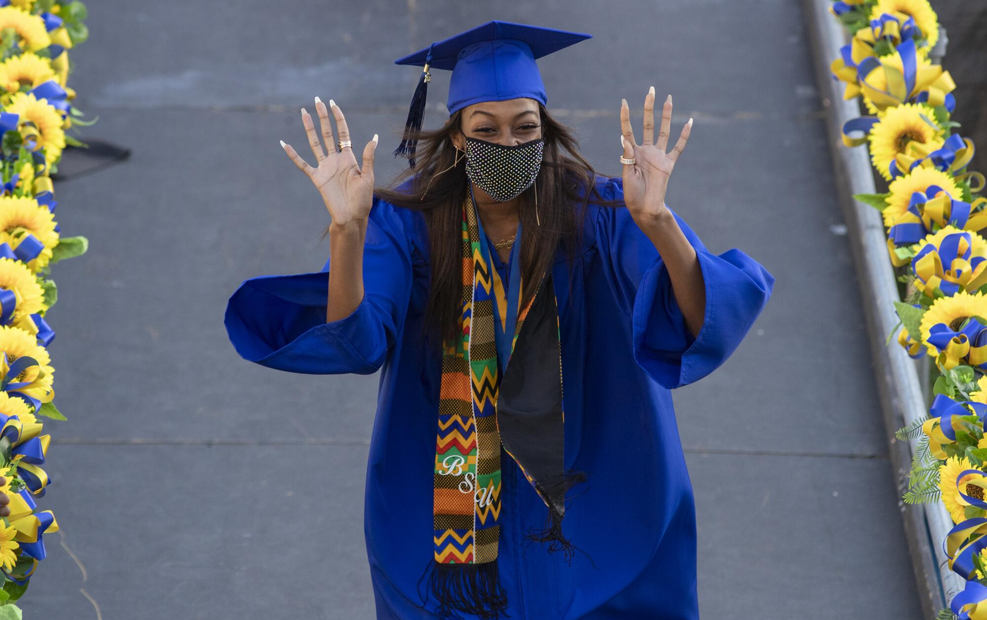 A student in cap and gown waves with both hands.