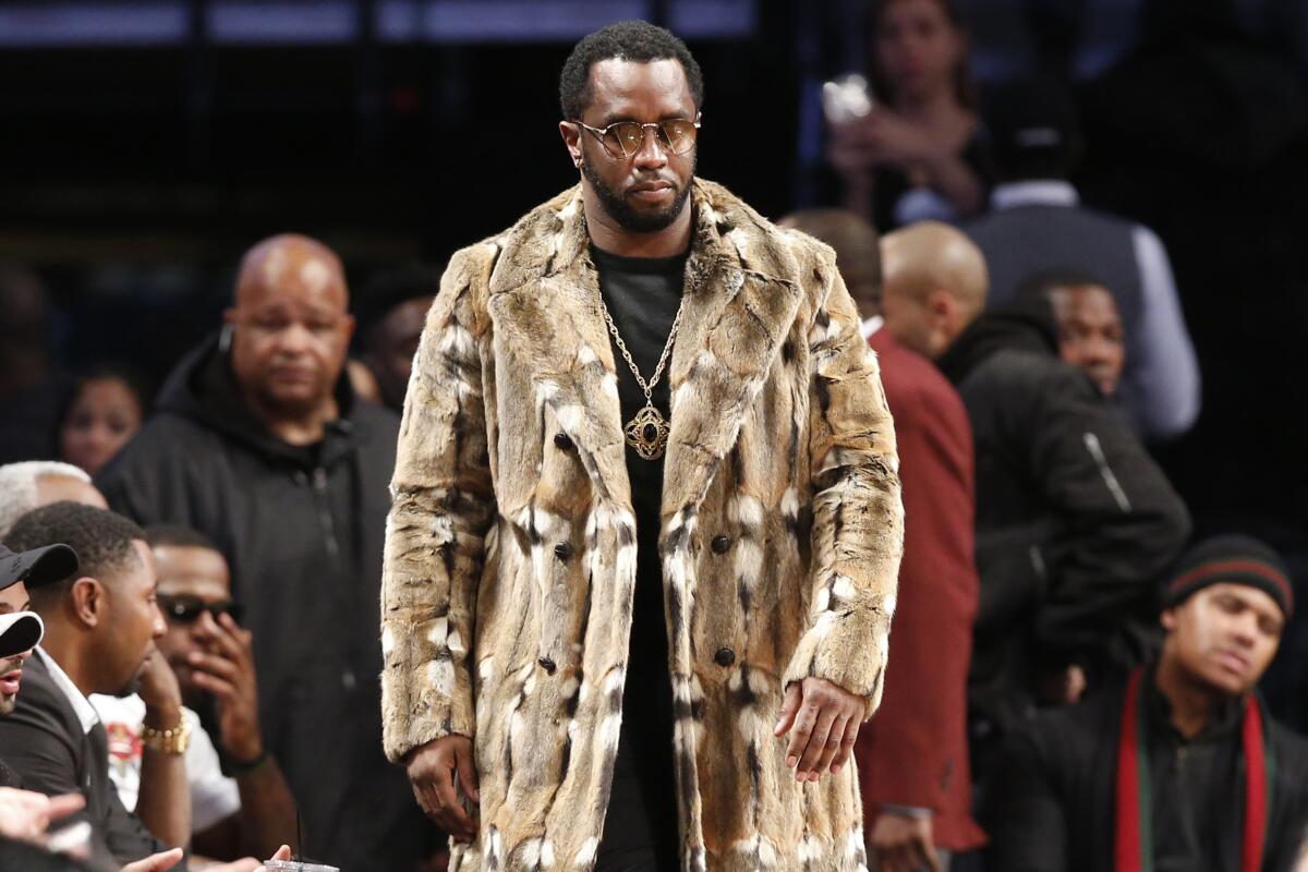 Sean "Diddy" Combs, wearing a fur coat, walks down the sideline of an NBA basketball game.