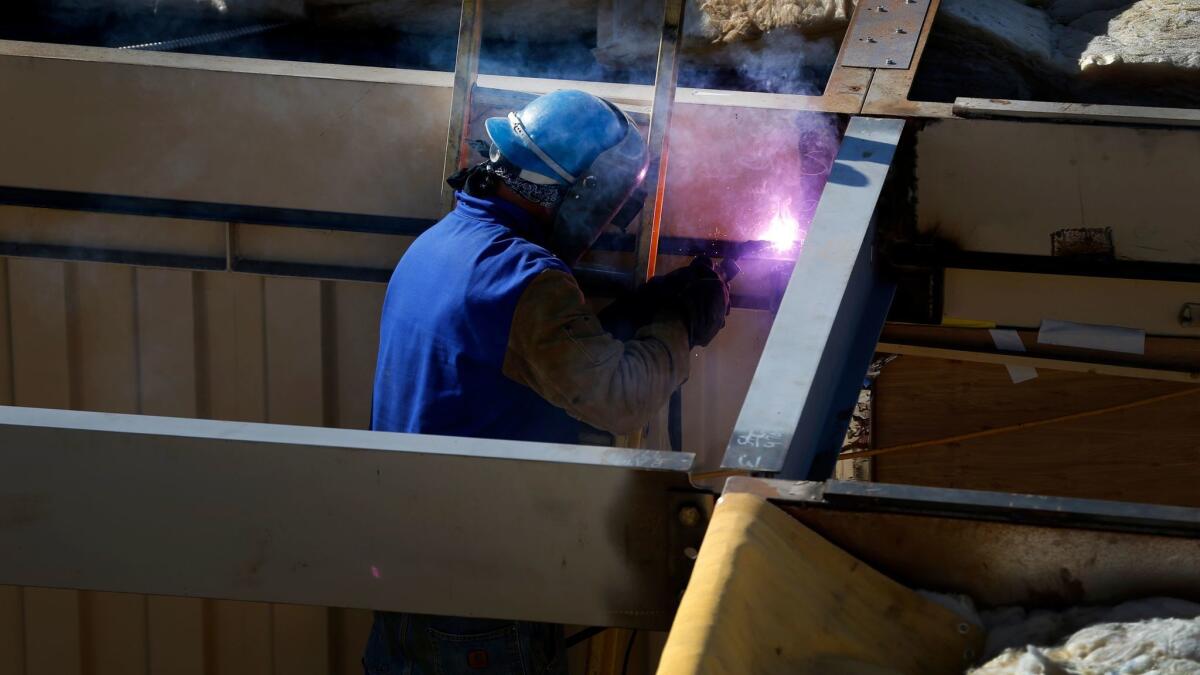 A worker welds together one of the two-story high pre-constructed shipping containers. Construction added the most jobs in the state last month.