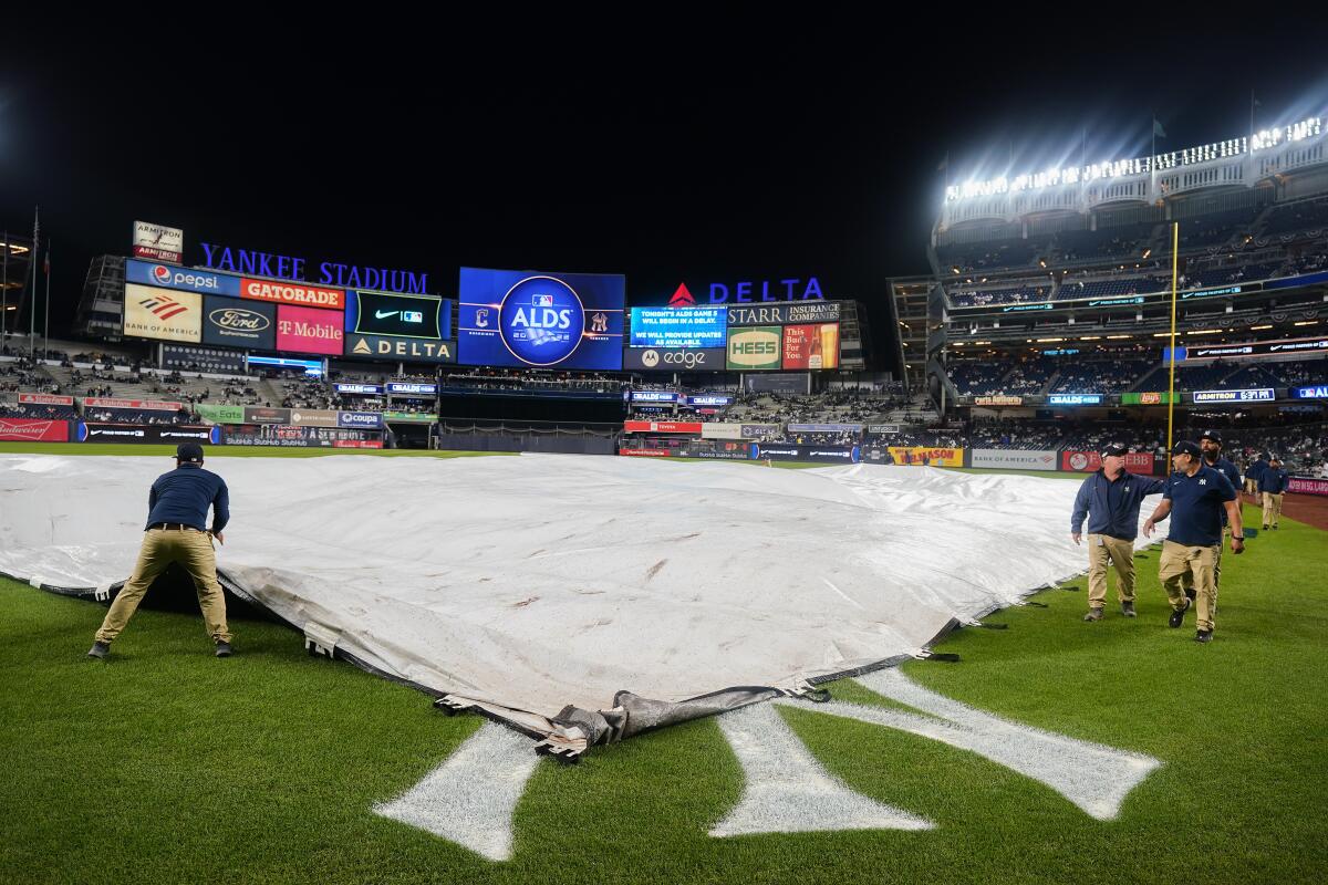 The Yankee Stadium grounds crew pulls the rain tarp over the field during a rain delay before Game 5 of an American League Division baseball series between the New York Yankees and the Cleveland Guardians, Monday, Oct. 17, 2022, in New York. (AP Photo/Frank Franklin II)