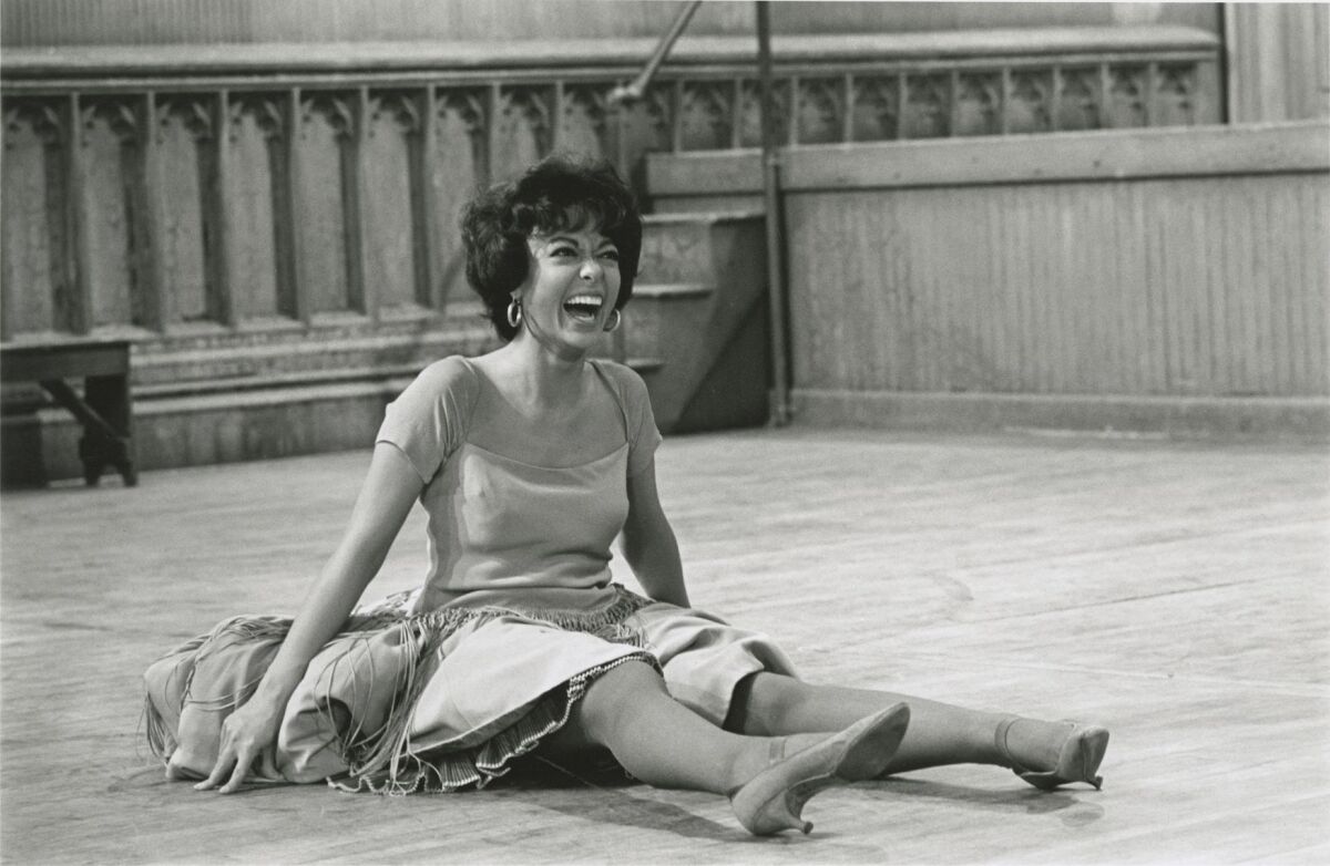 A smiling Rita Moreno sits on the floor on the set of "West Side Story."