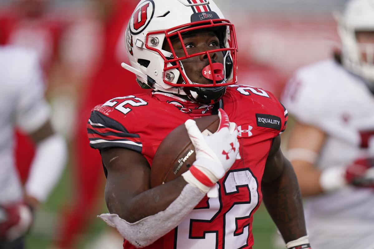 Ty Jordan, on the field in Utah uniform, carries the football in one hand as he runs.