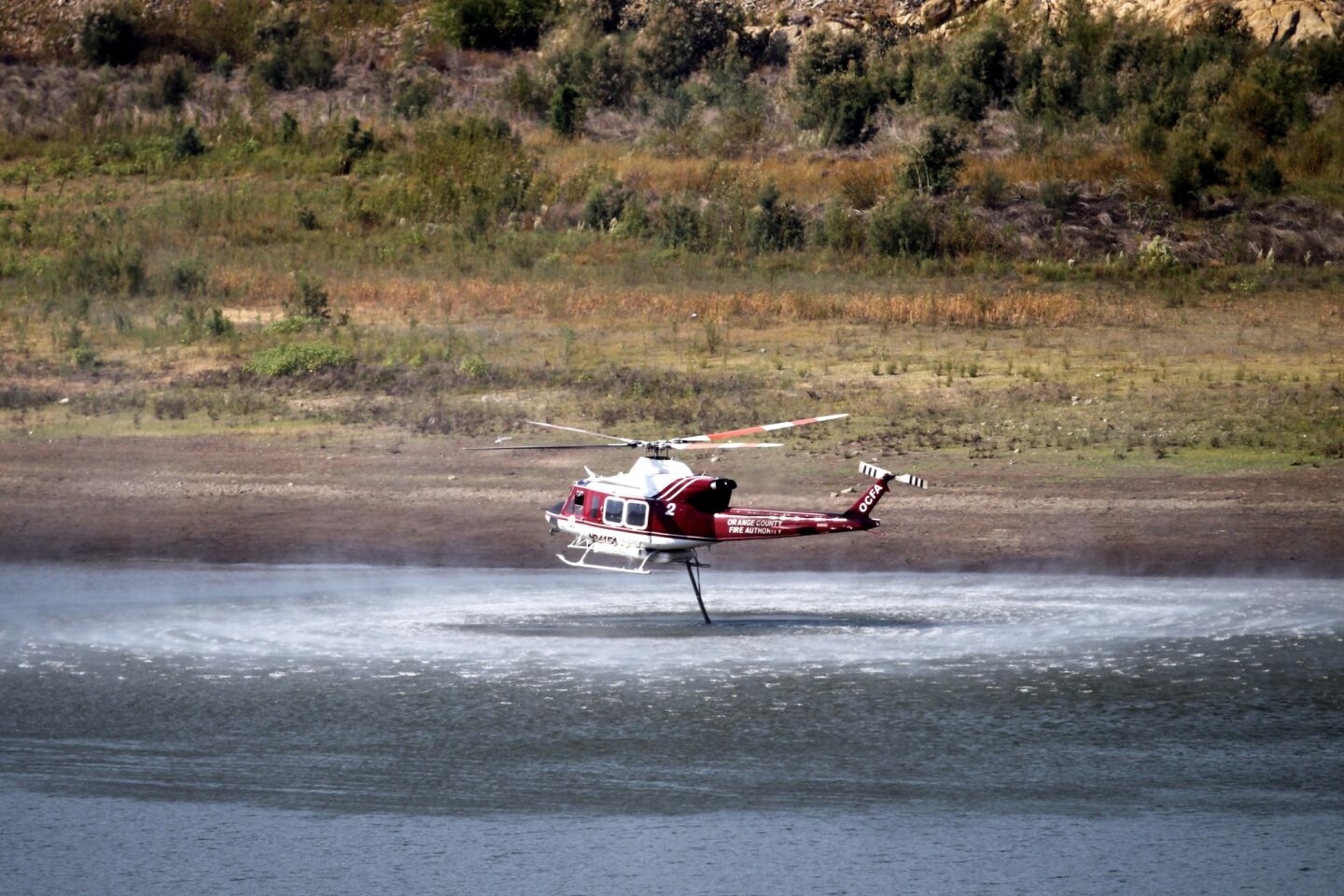 An Orange County Fire Authority helicopter takes on water from the drought-stricken Irvine Lake before making a water drop on a brush fire near homes on Silverado Canyon Road.