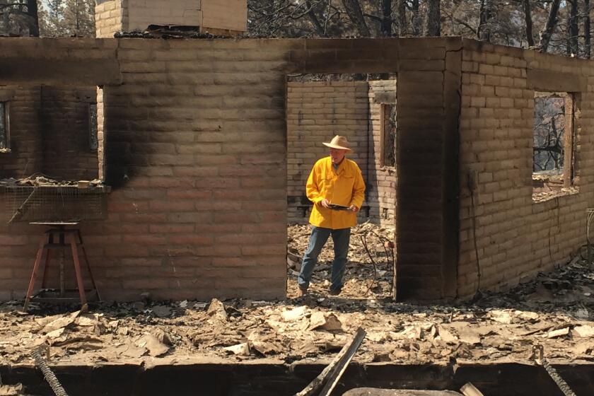 In this photo provided by Rusty Bowers, Arizona House Speaker Rusty Bowers walks through the remains of his family's weekend home on Tuesday, June 8, 2021, that was destroyed by a wildfire the day before. Bowers used the home in the remote mountains as a family retreat and often did his artwork there. (Elijah Cardon/Rusty Bowers via AP)