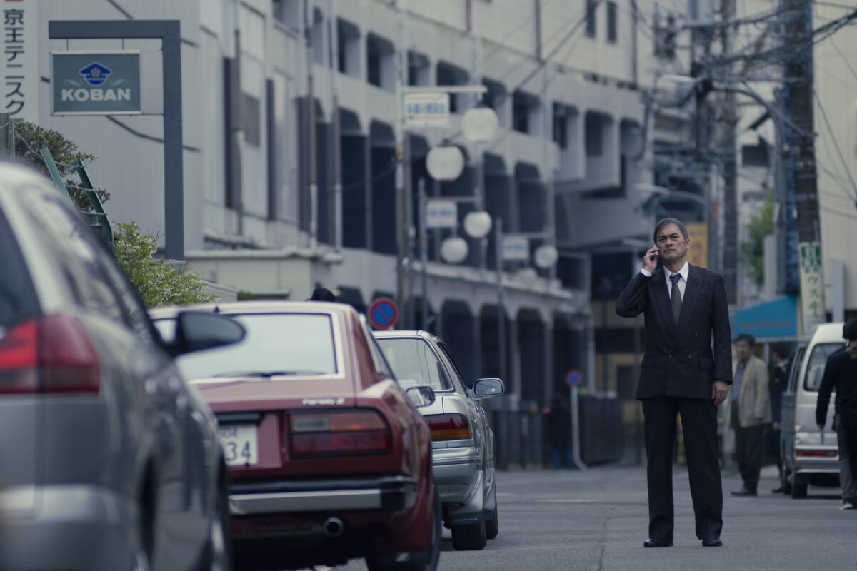 A man stands in the middle of the street in a suit, talking on a cellphone. 