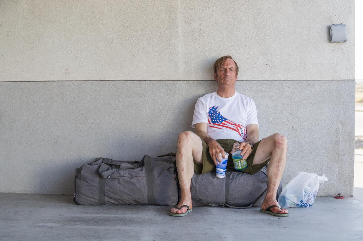 A man sitting on a duffel bag double-fisting drinks and looking exhausted