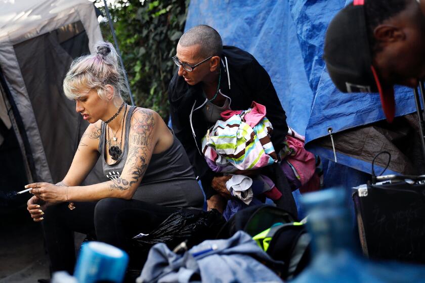 Two women, one pregnant, outside tents with a man visible in the foreground.