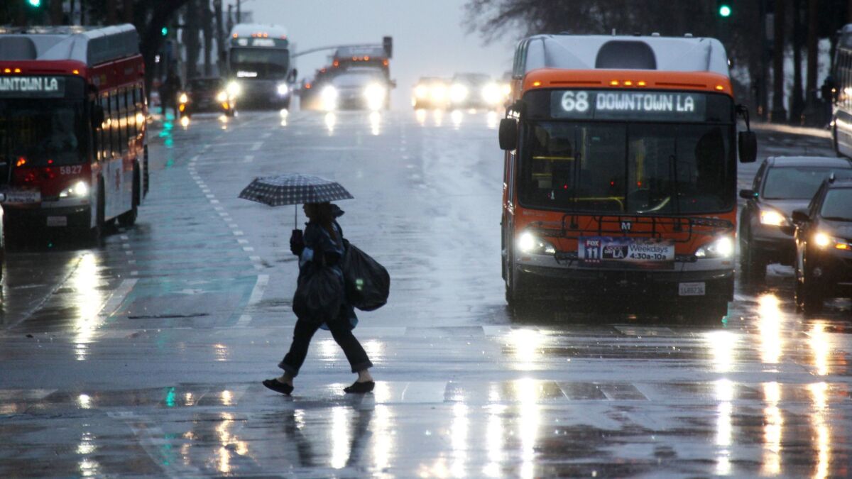 A pedestrian crosses a downtown Los Angeles street on a rainy Friday in January.